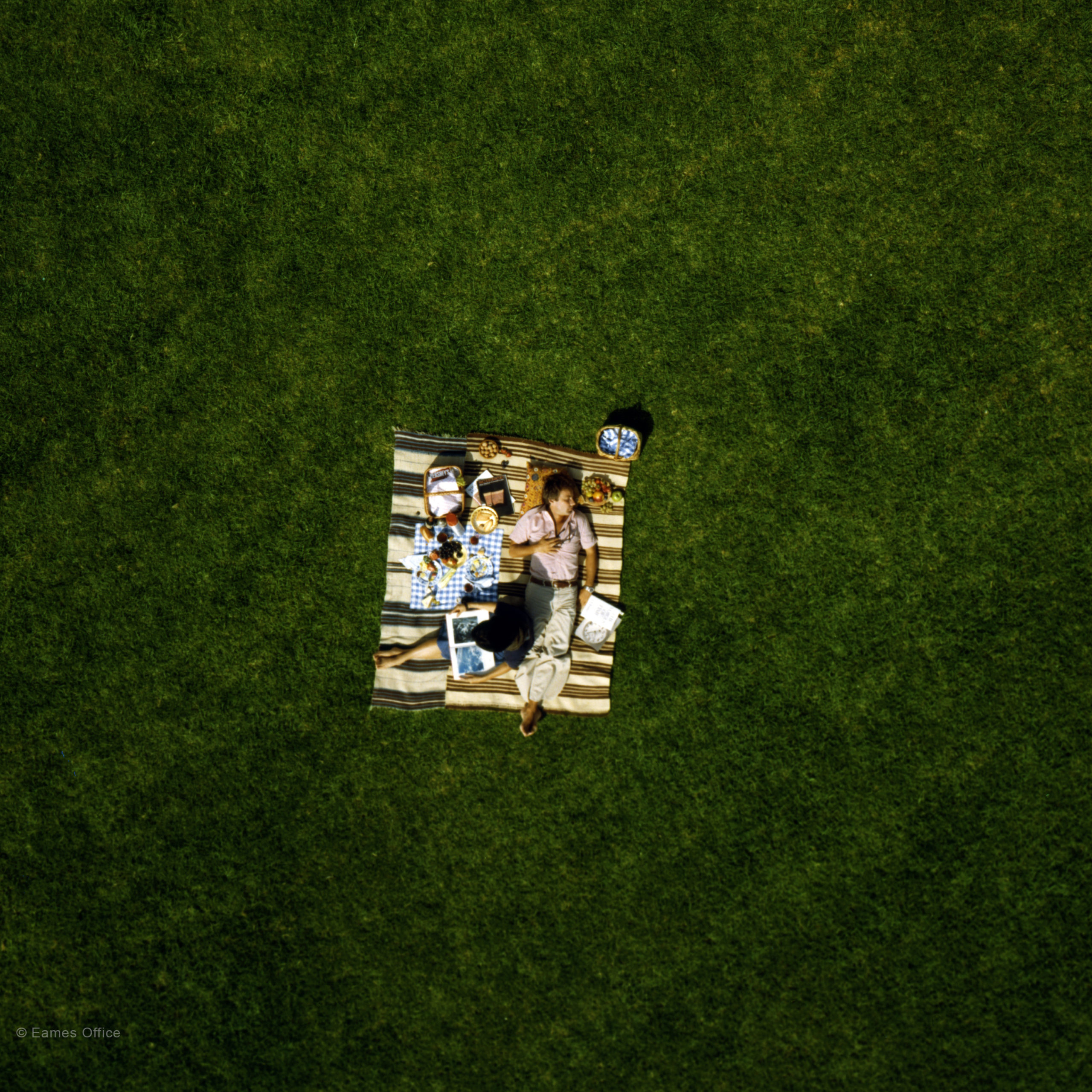 Bird's eye view from about 10m up of a couple having a picnic in the park. The man is lying down, snoozing.